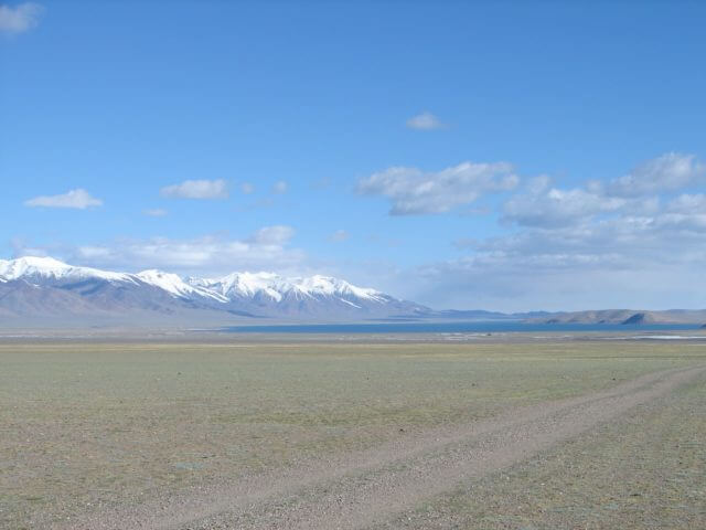 Wide plains with snowcapped mountains and a lake in the background.