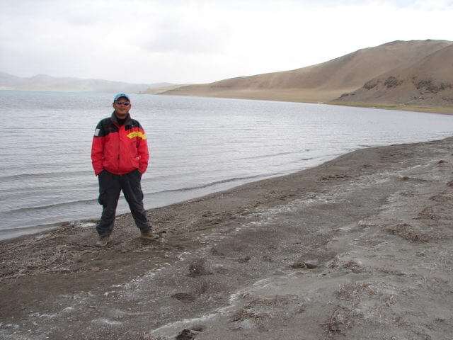 A man in a red coat standing by the lake Aru Tso