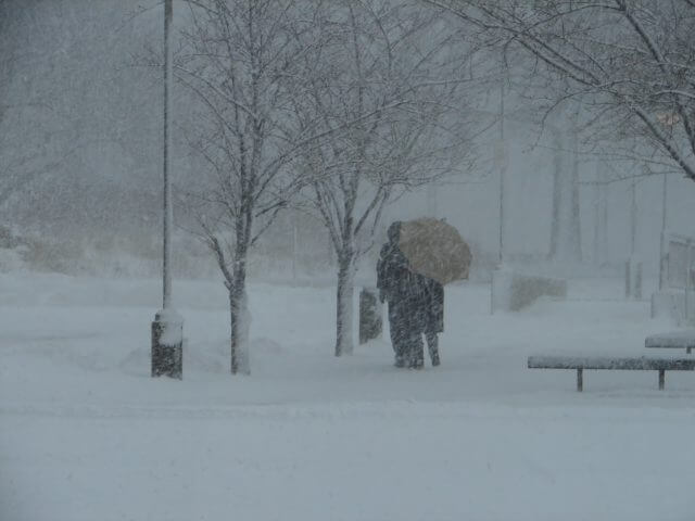 People walking in a snowstorm with an umbrella.