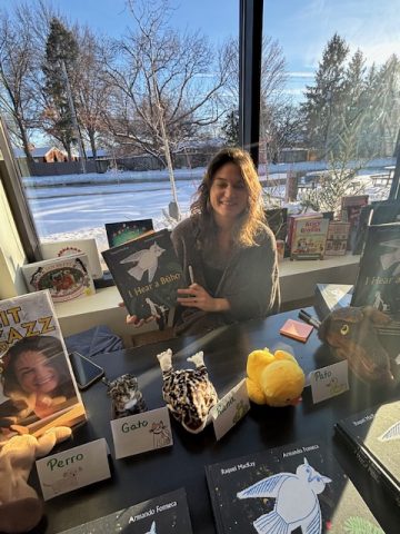 Author Raquel Mackay sitting at a table with her books displayed around her