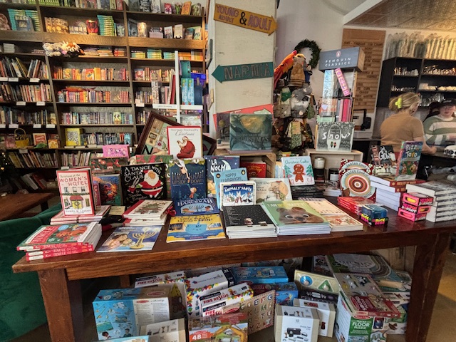 A table full of books for sale, in the background are many bookshelves filled with books.
